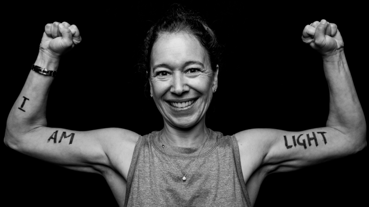 Coach Ali Levin flexing her arms, on which is written "I AM LIGHT"
