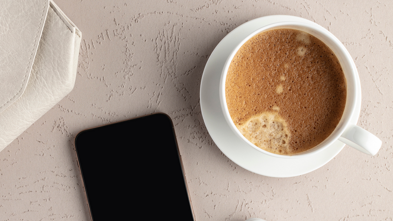 A coffee, cellphone, and handbag on a textured tabletop