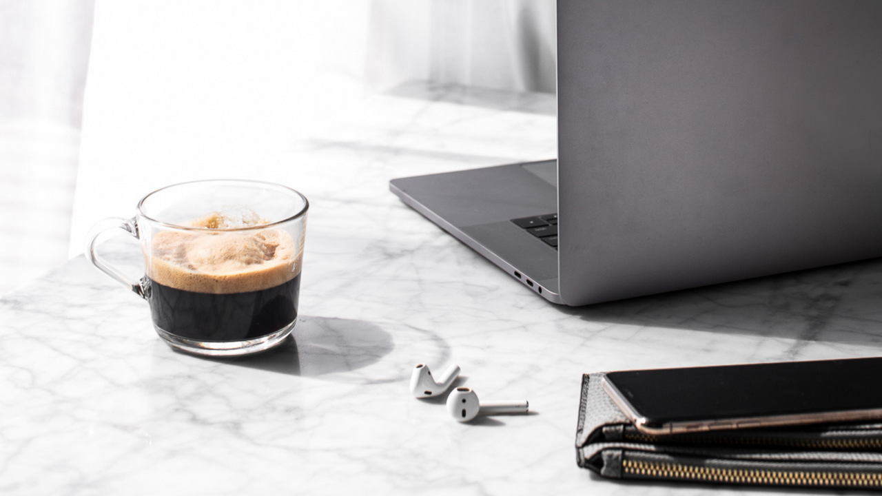 A coffee, laptop, phone, purse, and pair of airpods on a marble tabletop